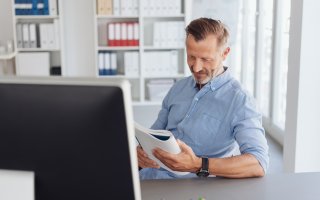Un homme lit un rapport devant son bureau 