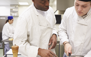 Photo d'un jeune en formation cuisine avec son chef à côté de lui